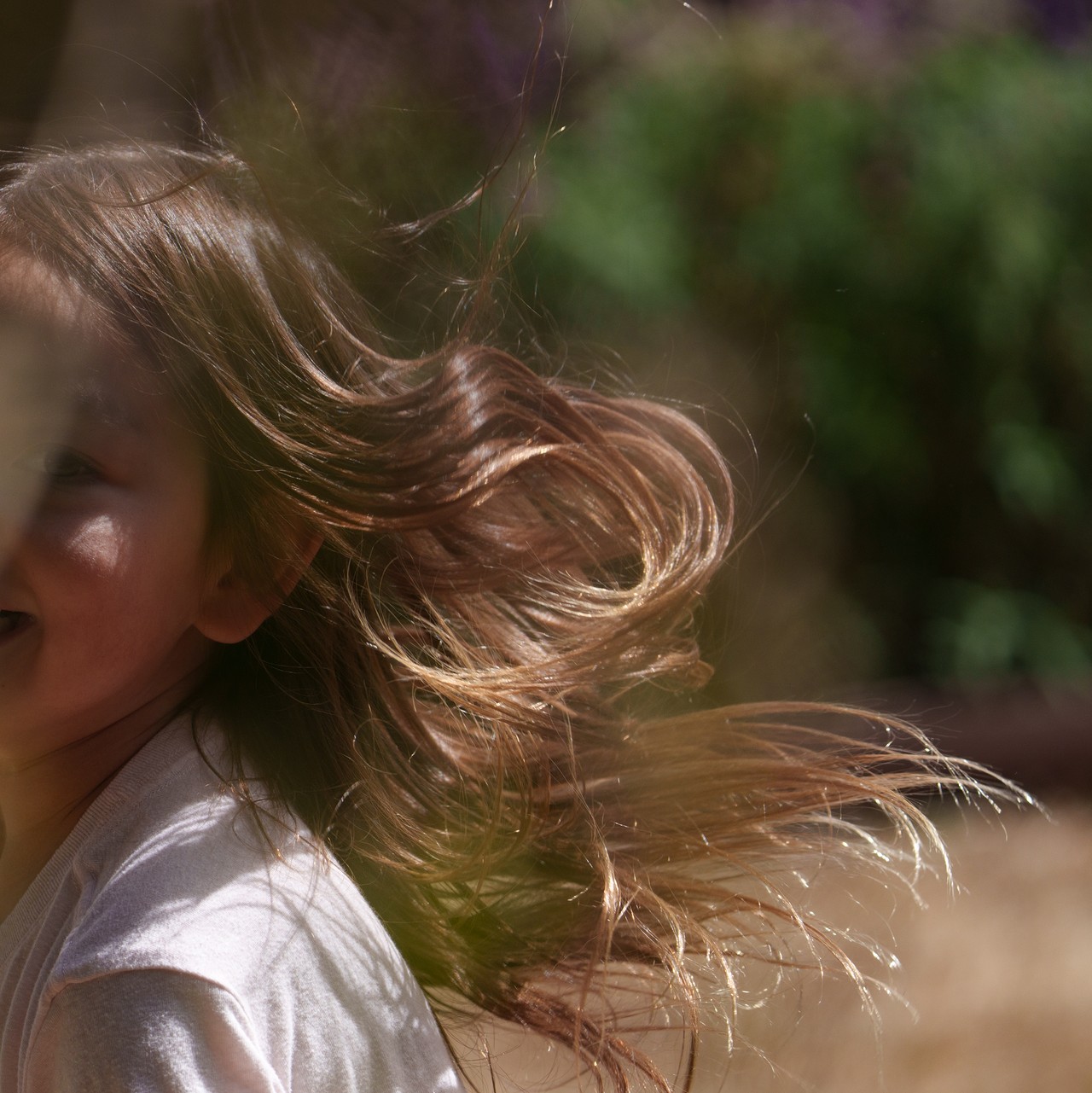 Child laughing with hair caught mid-flight in bright sunlight, garden behind