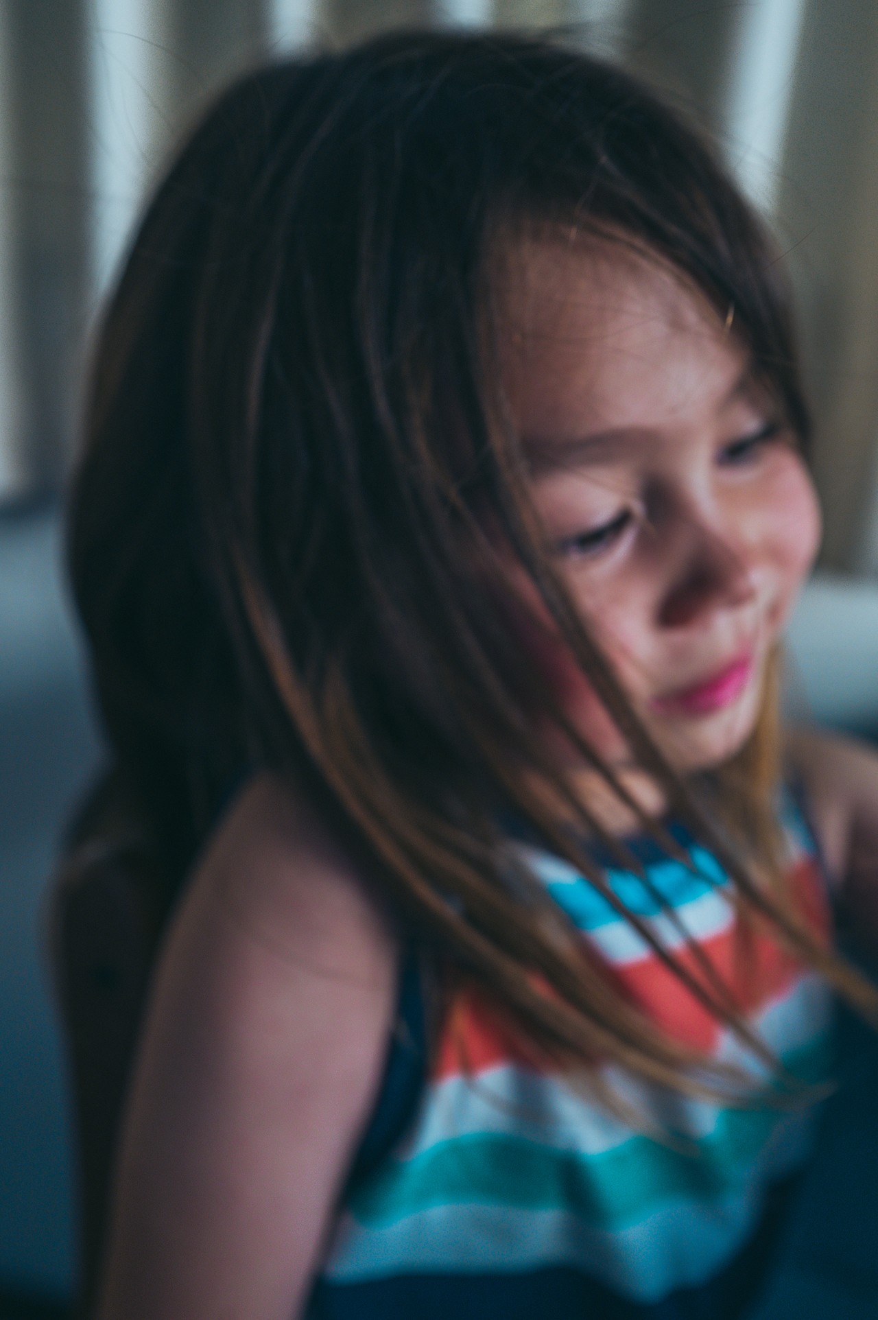 Child with hair falling across her face, soft focus, indoor light
